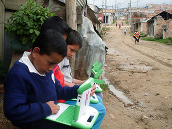 dirt road, tin housing, boys using special computer'